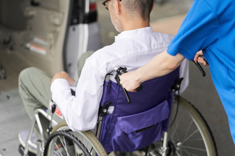 A caregiver assisting a disabled individual into a transport vehicle for mediation, ensuring comfort and support.