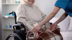 Nurse gently covering with blanket woman in wheelchair, care about old people