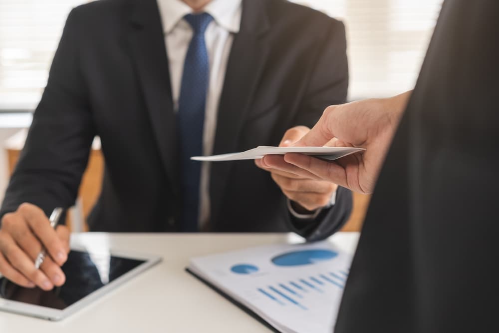 manager hands bonus envelope to employee as reward for good performance.